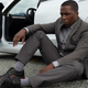 Leslie Odom Jr. wearing a suit and sitting next to a car, looking worried, in time-travel tale Needle in a Timestack.